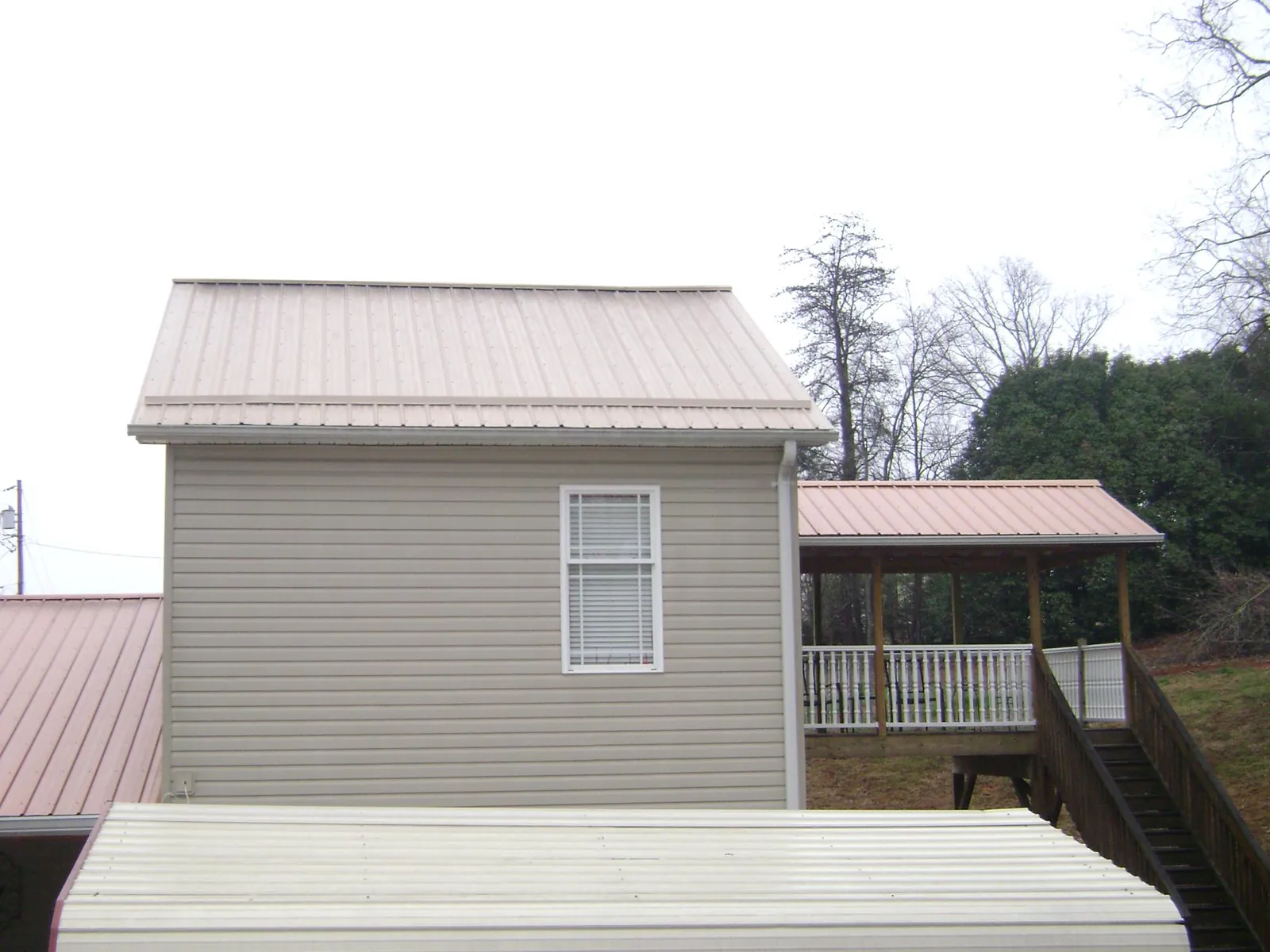 Tan metal roofs on a two story addition and attached porch, from a Roof Replacement job in Gaston